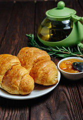 fresh croissants with jam on dark wooden table and tea with rosemary,