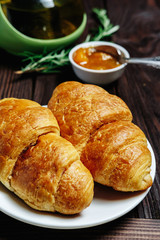 fresh croissants with jam on dark wooden table and tea with rosemary,