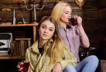 Friends on calm faces in plaid clothes relaxing. Girls relaxing and drinking mulled wine. Friends in casual outfits enjoy warm atmosphere, wooden interior. Holiday and vacation concept