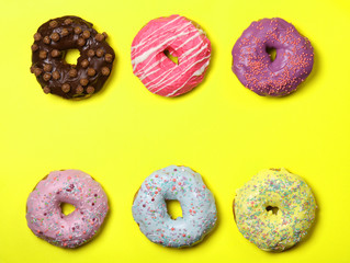 Many multicolored donuts on a yellow background. Frame, space for text