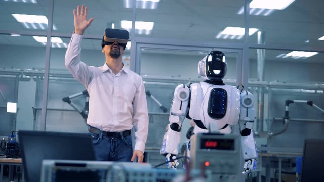 Male worker and robot make movements with arms. Virtual reality game.