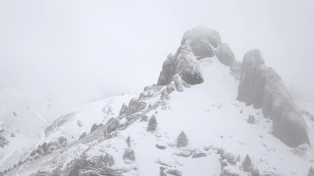 Aerial flying around rocky peak in Carpathians during a cold foggy winter day. Snow covered mountain