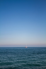 Fototapeta premium Sea water landscape with dark waves and a lonely white and red yacht at the horizon on sunny day.