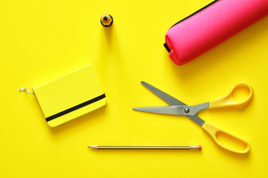 School Tools Such As Yellow Scissors, Pencil, Ruler, Eraser, And Pencil Case, Over A Yellow Flatlay In Blue From Above