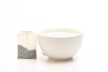 Mug filled with boiling water and teabag on white background. Cup or white porcelain mug with transparent hot water and dry bag of tea near. Tea time concept. Process of tea brewing in ceramic mug