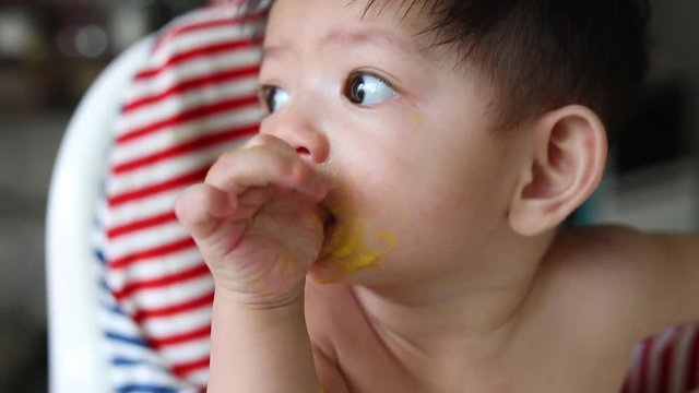 cute baby sucking thumb finger hand with puree mess on face