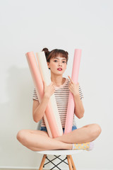 Portrait of a pretty woman in striped shirt holds drawings in rolls she is smiling while sitting on chair over white background and looking at camera