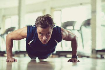 Portrait shot of handsome young athlete looking at camera while doing push-ups at spacious gym with panoramic windows