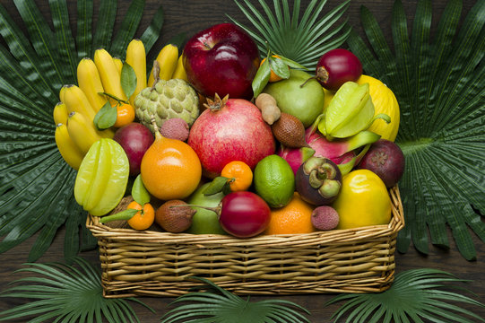 Fresh Thai fruits in wicker basket on palm leaves and wooden background, healthy food, diet nutrition 