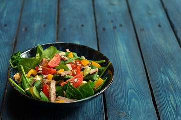 Salad with spinach, tomatoes and peppers in a bowl on a wooden background