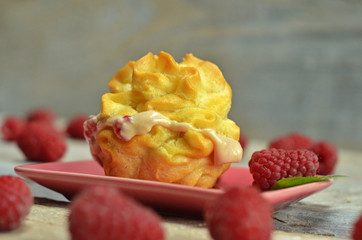 Puff with raspberry cream on a pink saucer on a wooden background