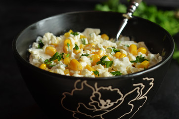 Raw cauliflower salad with corn in a black bowl