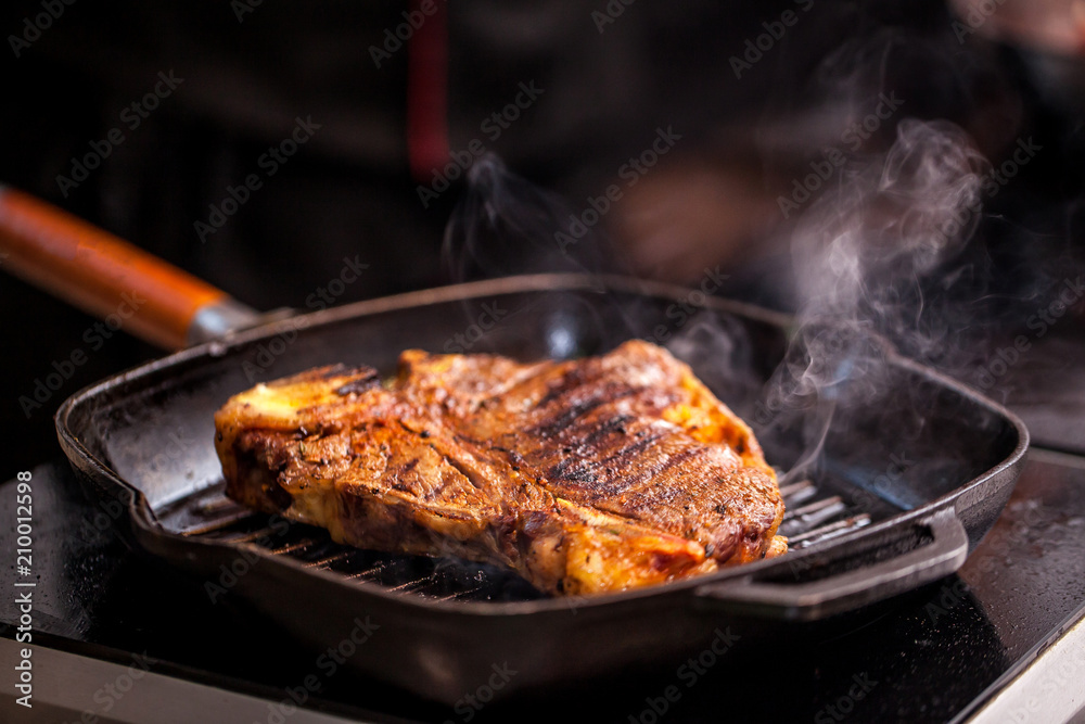 Wall mural Concept of the correct cooking of meat. The chef prepares, fries a steak of mutton, pork or veal in a frying pan on an induction cooker, with the addition of spices, marinade and wine. Selective focus