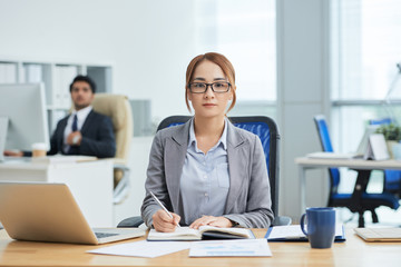 Fototapeta na wymiar Portrait of Asian businesswoman in eyeglasses sitting at her workplace