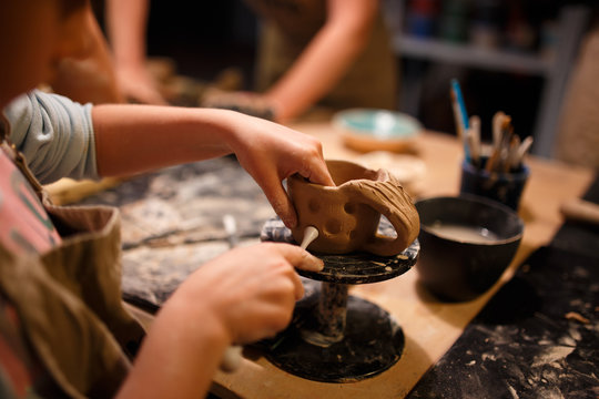 Child girl making a cup from red clay at pottery workshop