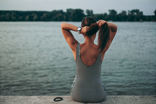 Girl tying her hair while sitting by the water
