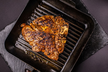 Fried chunk of meat, a beef steak, pork or veal, lamb, lies on a black grill pan, on a black slate. Next to the meat are spices and vegetables. Top view. Copy space