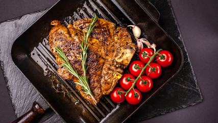 Fried chunk of meat, a beef steak, pork or veal, lamb, lies on a black grill pan, on a black slate. Next to the meat are spices and vegetables. Top view. Copy space