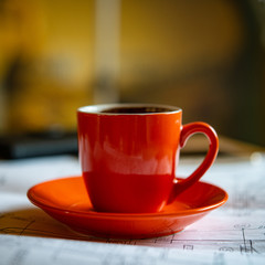 orange cup of fresh brewed hot coffee stands on drawings and a smartphone.