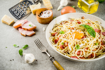 Traditional italian pasta, spaghetti carbonara with bacon, creamy sauce, parmesan cheese, egg yolk and fresh basil leaves grey stone background copy space