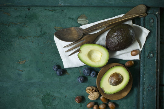 Cloth, salad cutlery, avocados, blueberries and nuts on green ground
