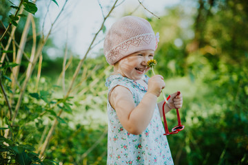 A little girl sniffs a yellow dandelion and laughs. Blurred green park background