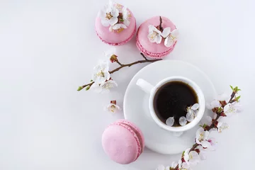 Keuken spatwand met foto Pink macaroons with a cup of coffee and a branch of white flowers on a white background. French dessert and flowers blooming cherry. Sakura flowers with pink macaroon close up. © Alina