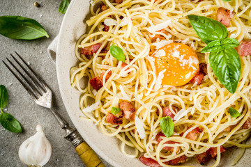 Traditional italian pasta, spaghetti carbonara with bacon, creamy sauce, parmesan cheese, egg yolk and fresh basil leaves grey stone background copy space
