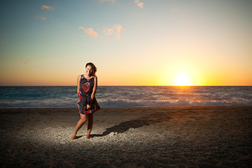 Fototapeta na wymiar Young woman standing on the beach on sunset