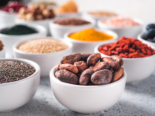 Raw cocoa bean in small white bowl and other superfoods on background. Selective focus. Different superfoods ingredients. Concept and illustration for superfood and detox food