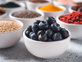 Blueberries in small white bowl and other superfoods on background. Selective focus. Different superfoods ingredients. Concept and illustration for superfood and detox food