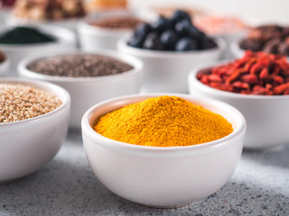Turmeric powder in small white bowl and other superfoods on background. Selective focus. Different superfoods ingredients. Concept and illustration for superfood and detox food
