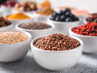 Flax sseds in small white bowl and other superfoods on background over gray concrete background. Selective focus. Different superfoods ingredients.Concept and illustration for superfood and detox food