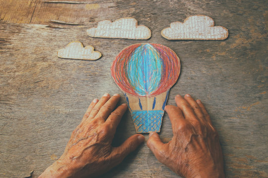 A close up of an elderly man holding a paper air baloon on a wooden table. Concept of thinking about childhood dreams, sadness and loneliness.
