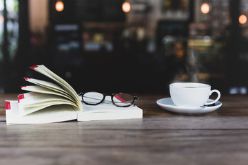 Selected focus of coffee cup with open book and glasses on wooden table