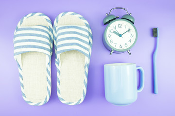 home equipment clock flat lay composition tooth brush glasses, towel and slippers top view on blue and purple violet concept.