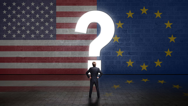 Geschäftsmann steht vor Wand mit den Flaggen von USA und EU und einem Fragezeichen