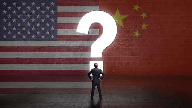 Geschäftsmann steht vor Wand mit den Flaggen von USA und China und einem Fragezeichen