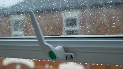 Large rain drops strike open window pane during heavy shower in England