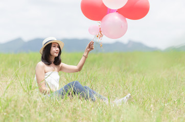 Young hipster girl holding balloon sit on the grass,