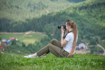Girl with camera sits on a hill and mountain photographs. Summer day