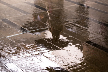 reflection of people with umbrellas in a puddle on the granite floor in the underpass