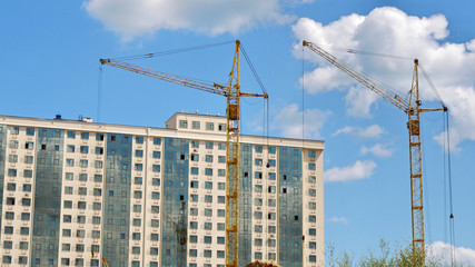 Fototapeta na wymiar two building cranes and a building under construction against blue sky. Construction site.