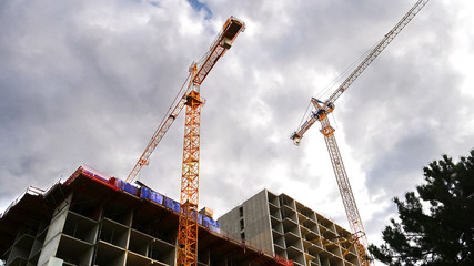 Two construction cranes near building under construction against blue sky. Construction site.