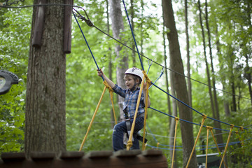 boy enjoys climbing in the ropes course adventure. smiling child engaged climbing high wire park.