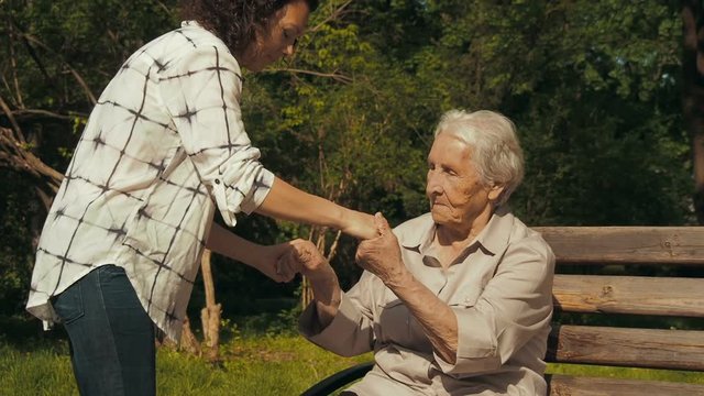 Help the elderly. The daughter helps the elderly mother to get up from the bench.