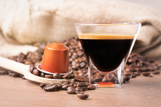 Cup of coffee with coffee capsule on wooden spoon, roasted coffee beans on wooden background,front view.
