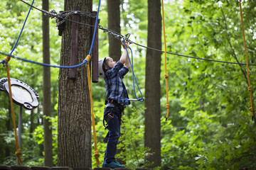 boy enjoys climbing in the ropes course adventure. smiling child engaged climbing high wire park.
