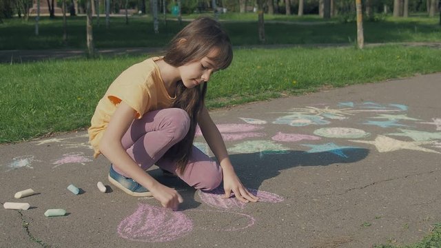 Little artist. The girl draws chalk on the asphalt.