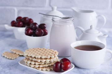 Breakfast. White cup of tea with thin waffles, lemon jam, yogurt and fresh fruit.
